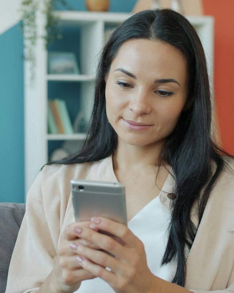 Vrouw kijkt glimlachend naar haar telefoon op de bank