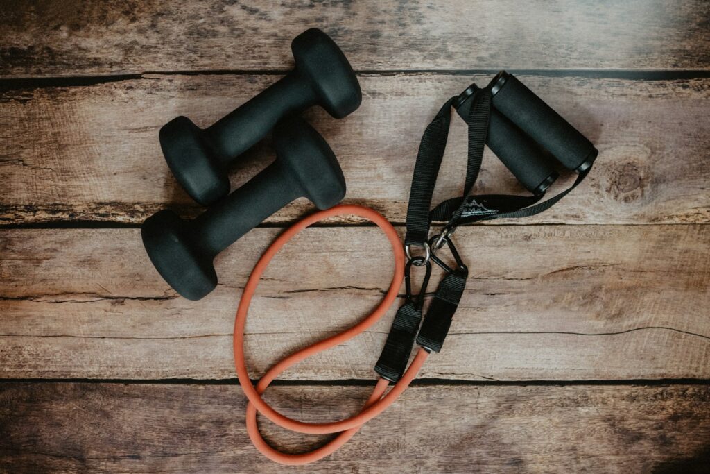 Een oranje weerstandsband met handvatten en twee zwarte dumbbells op een houten vloer
